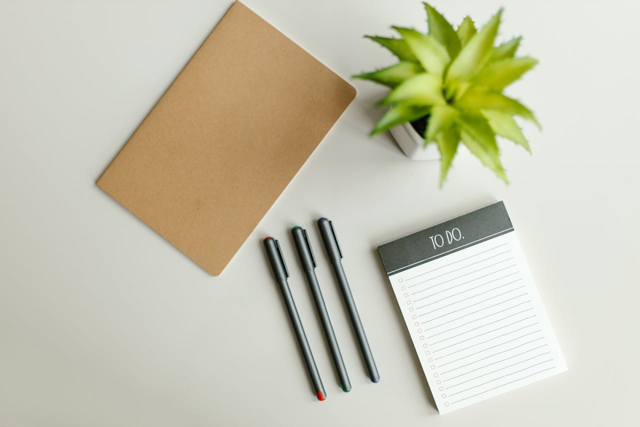 Home Flat lay of a to-do list, notebook, pens, and succulent on a light gray desk surface.